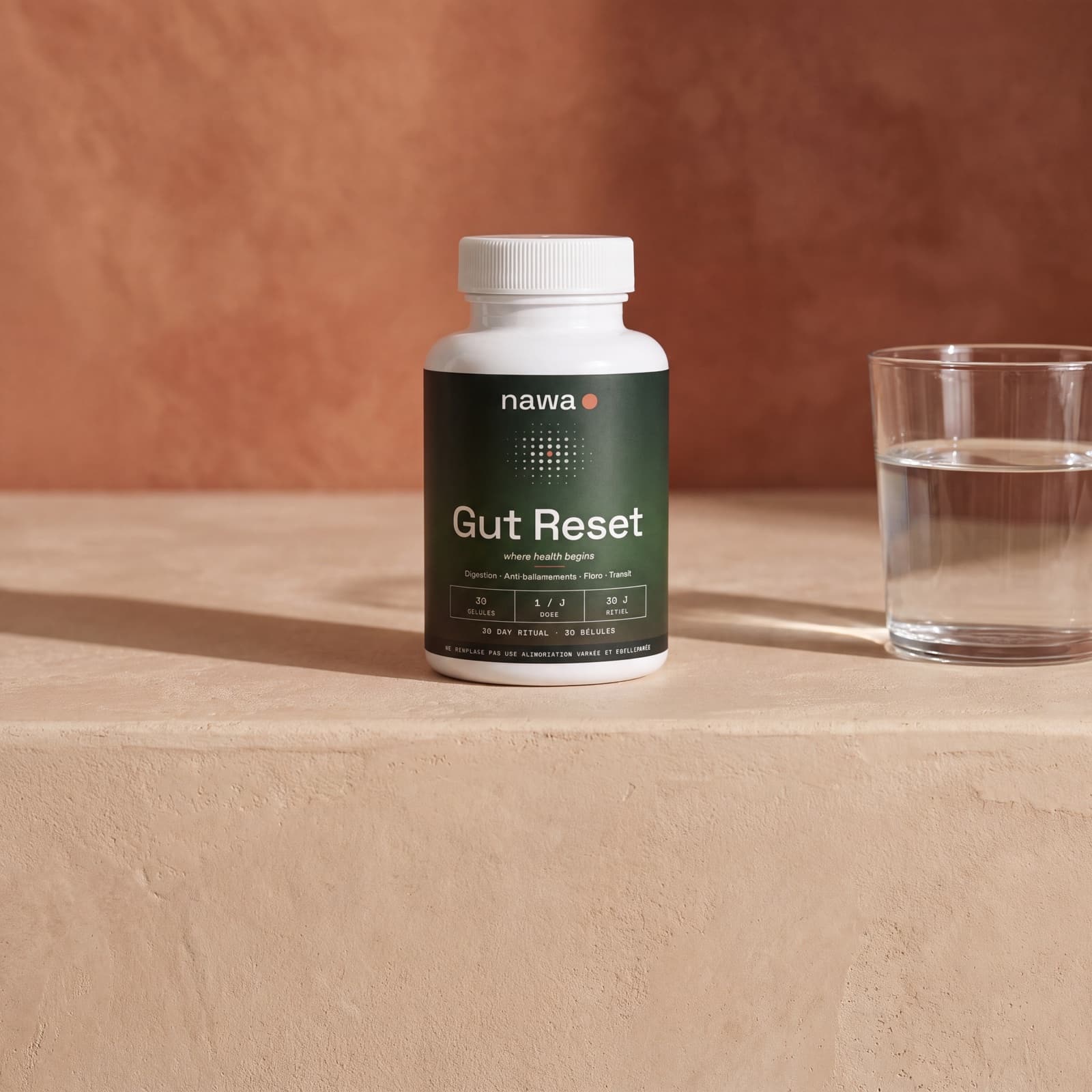 A NAWA Gut Reset bottle and a glass of water on a tadelakt surface, terracotta wall, morning light